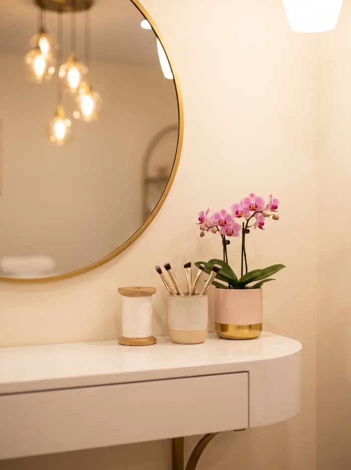 A gold-rimmed mirror, threading spool and brow brushes on a white vanity in a warm, softly lit brow studio